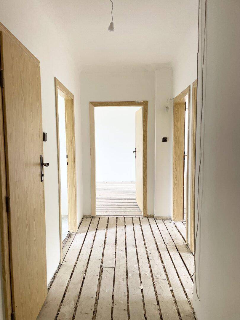Heller Flur mit freigelegten Holzdielen und mehreren Holztüren, die zu den Zimmern führen.
