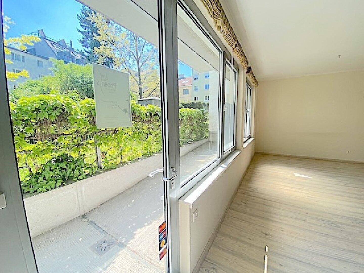 Große Fensterfront und Glastür bieten Zugang zu einem kleinen Außenbereich mit üppigem Grün.