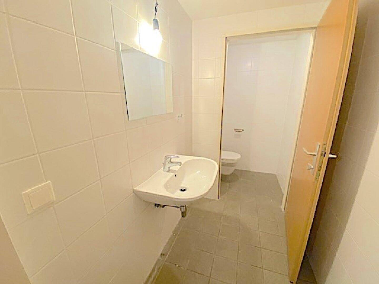 Helles Badezimmer mit modernem Waschbecken und Spiegel, angrenzend an einen separaten Toilettenraum.