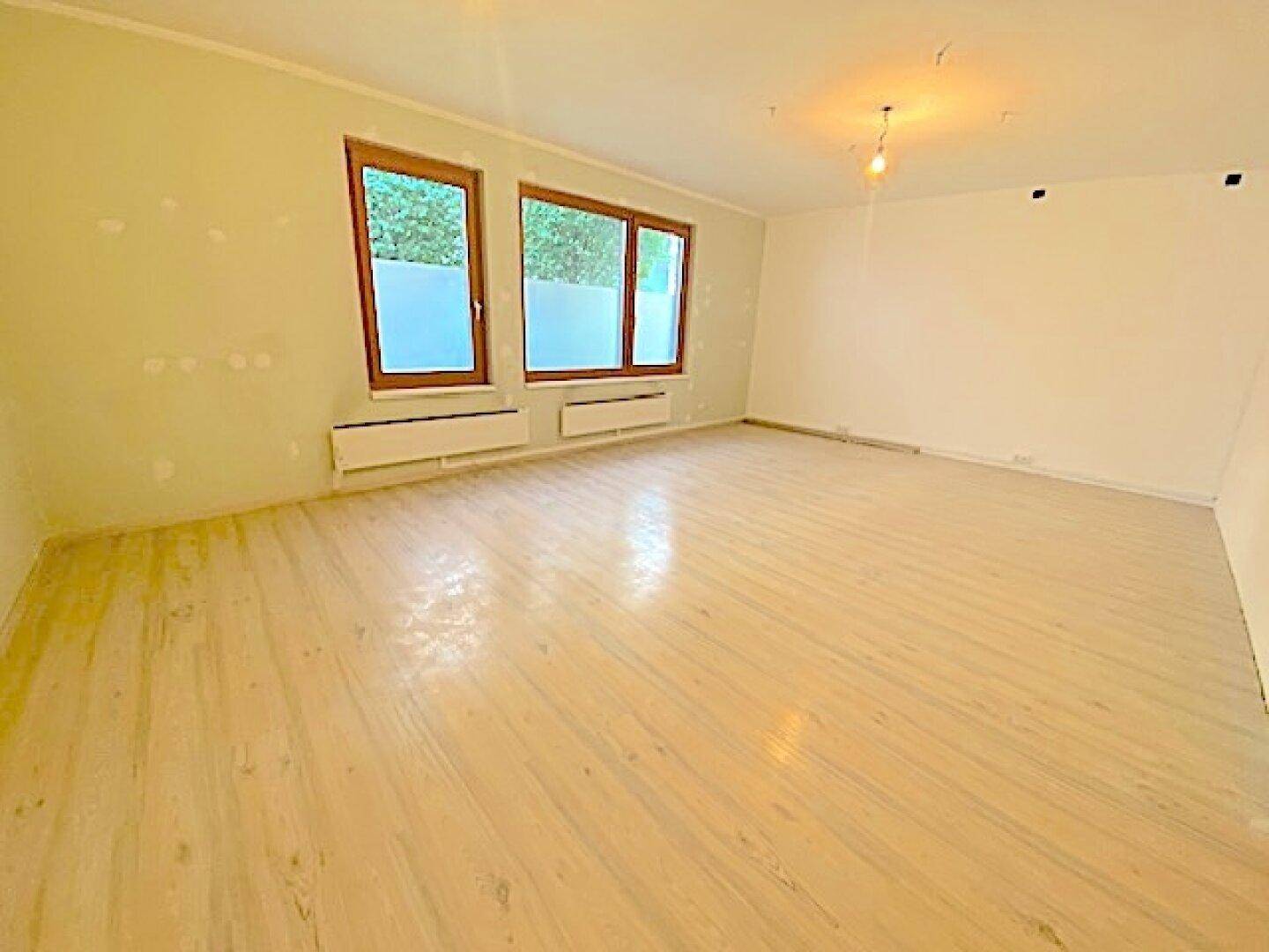 Heller, leerer Raum mit Holzfenstern und Heizkörpern, bereit für eine Renovierung.
