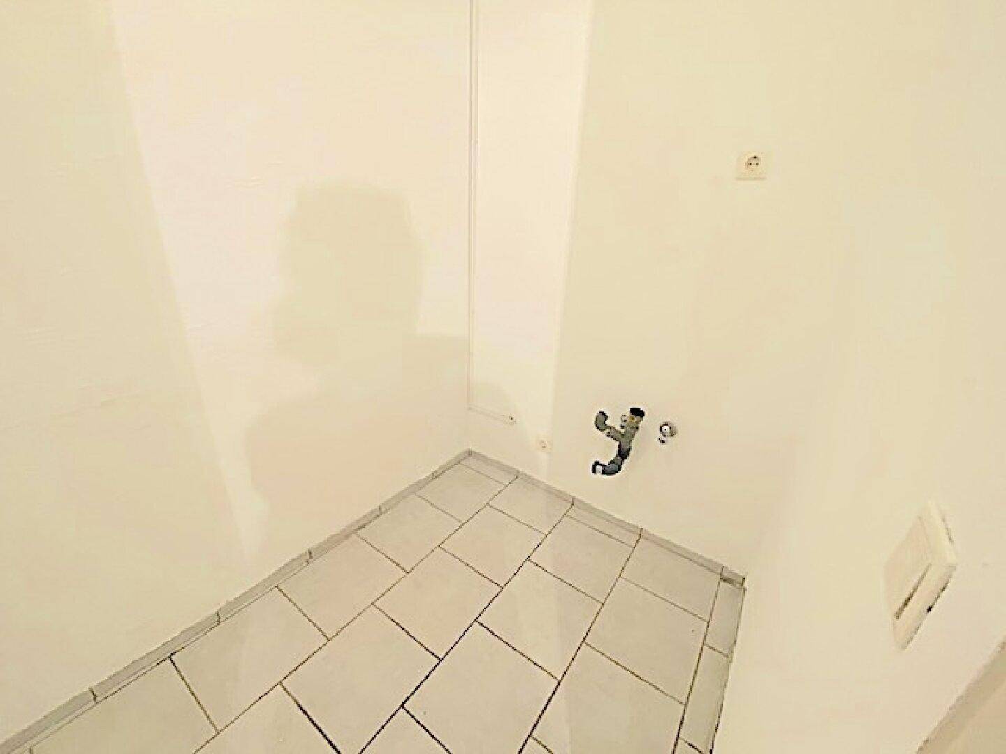 Kleiner Hauswirtschaftsraum mit gefliestem Boden und sichtbaren Anschlüssen an der Wand.