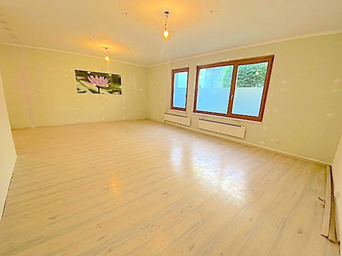 Geräumiger Raum mit hellen Wänden, Holzfenstern und einem dekorativen Bild an der Wand.