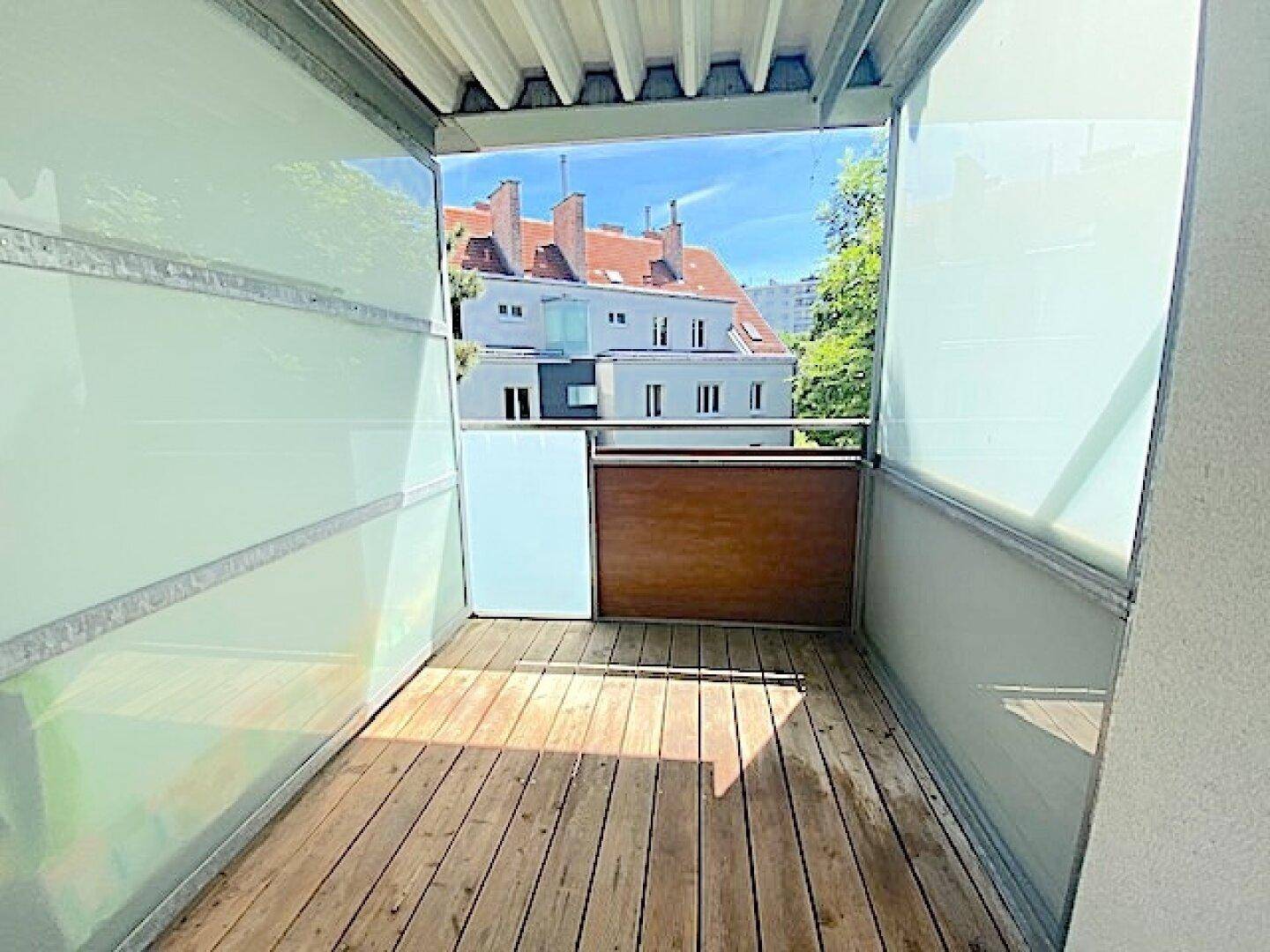 Balkon mit Holzboden und Milchglas-Seitenwänden, bietet einen Blick auf die Stadt.