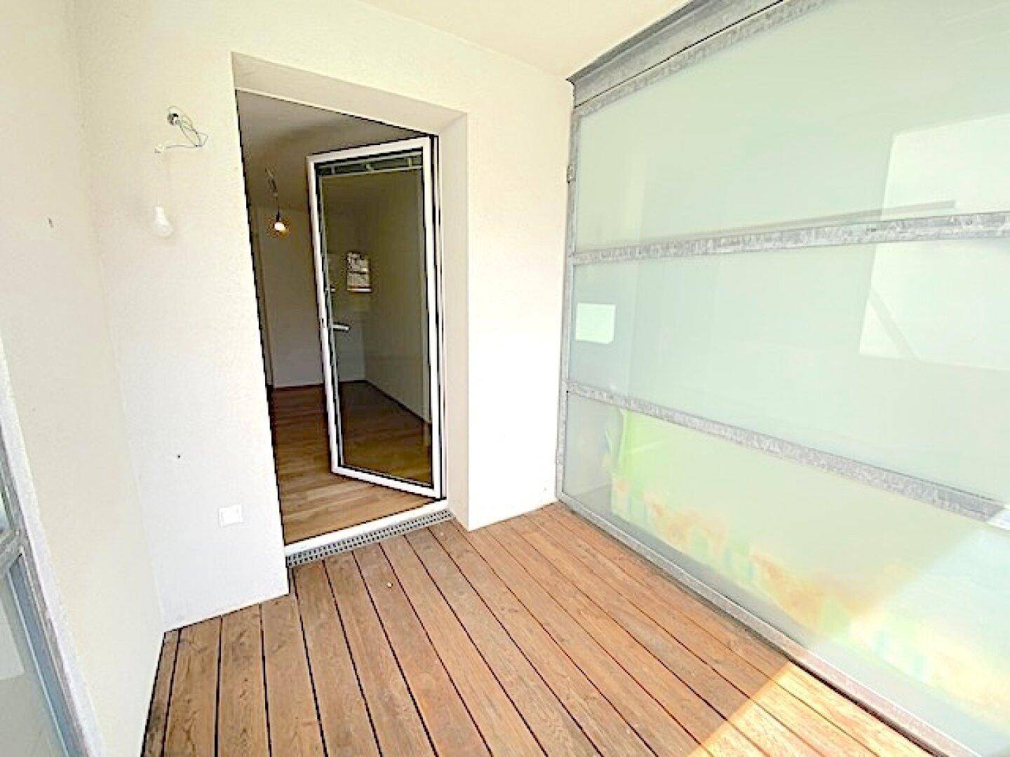 Balkon mit Holzboden und Milchglas-Seitenwänden, bietet direkten Zugang zum Innenbereich.