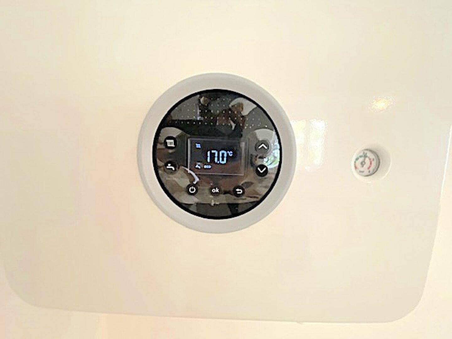 Modernes digitales Thermostat zur Steuerung der Raumtemperatur an einer weißen Wand.