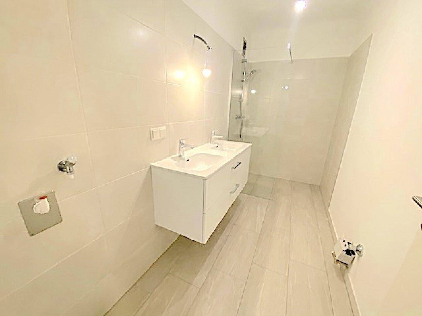 Modernes Badezimmer mit hellen Fliesen, Doppelwaschbecken und begehbarer Dusche.