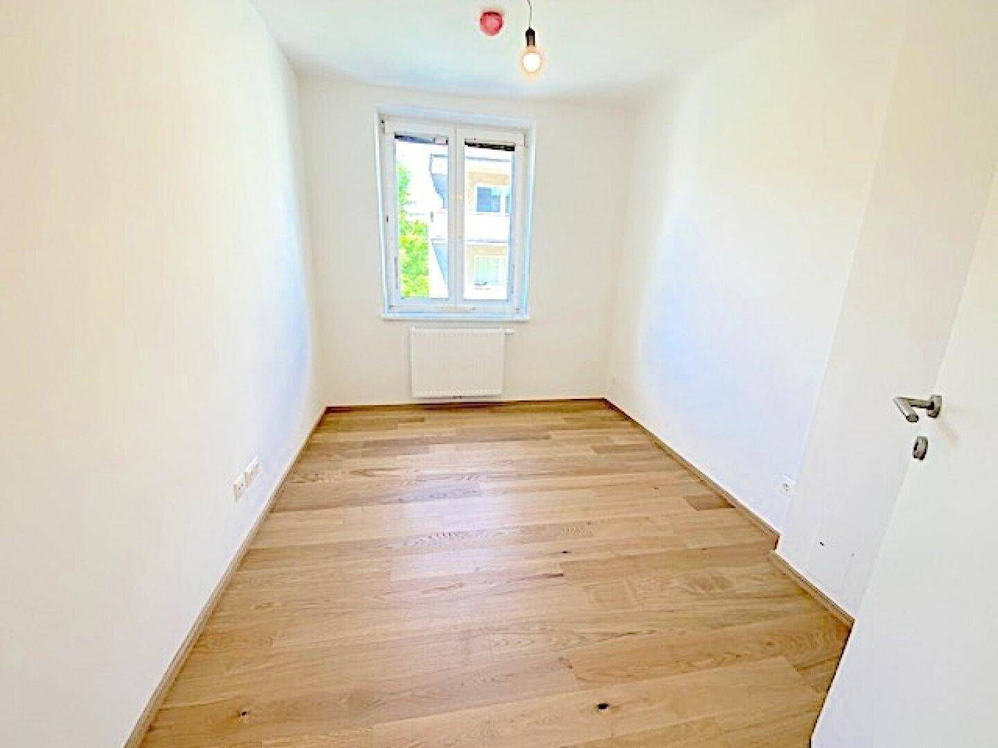 Helles, leeres Zimmer mit Holzboden und einem Fenster, ideal als Schlaf- oder Arbeitszimmer.