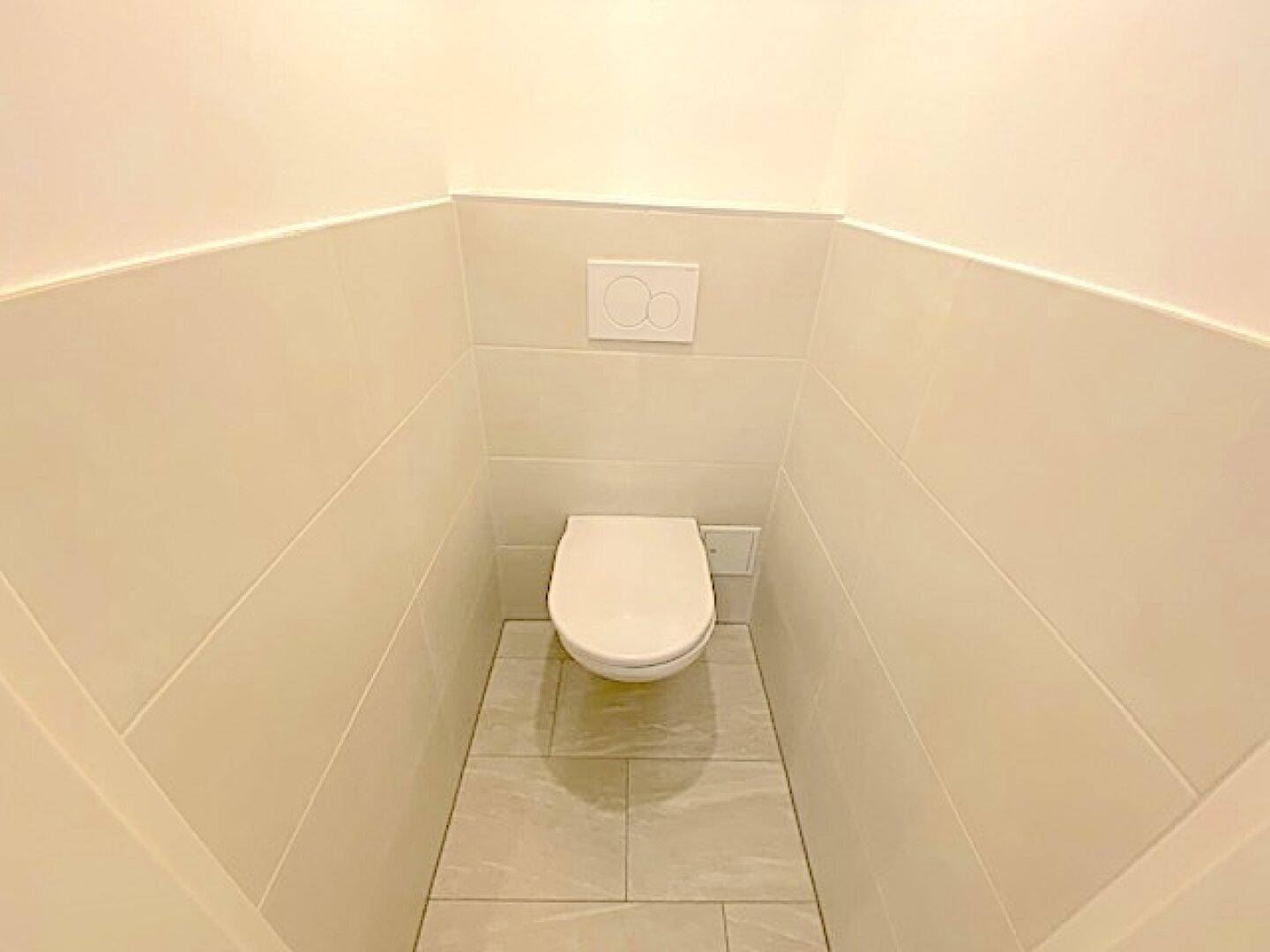 Separates WC mit wandhängender Toilette und hellen Fliesen, minimalistisch gestaltet.