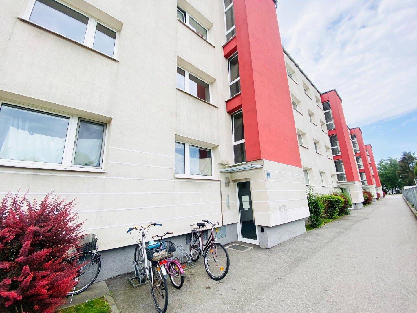 Moderne Wohnhausfassade mit roten Akzenten und Fahrradstellplätzen vor dem Eingang.