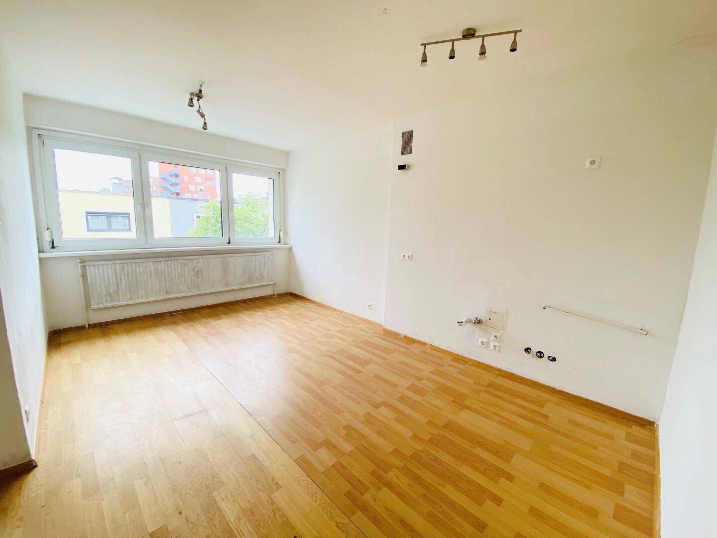 Helles Zimmer mit Parkettboden und Fenster, das einen Blick ins Grüne bietet.