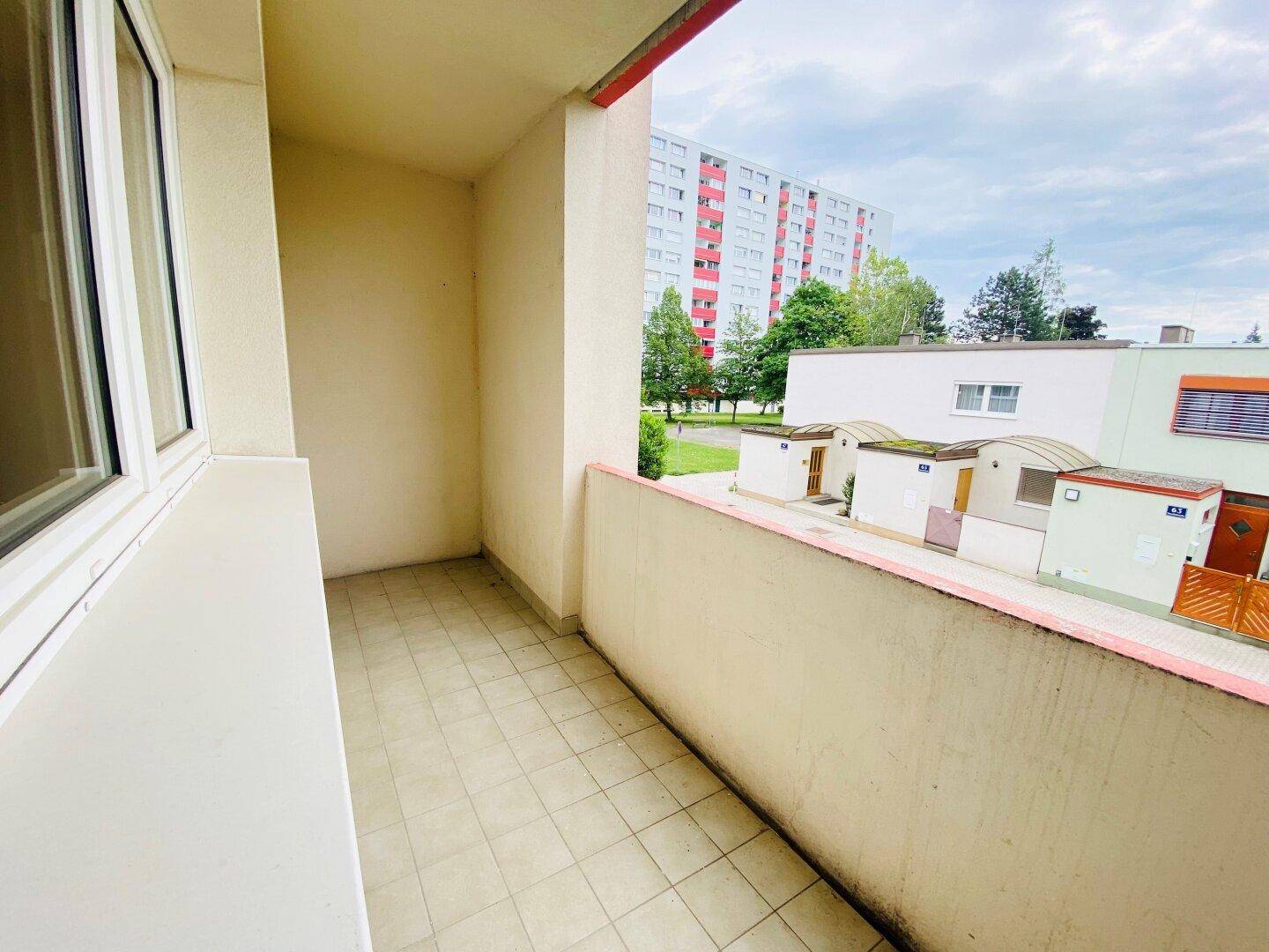 Balkon mit Fliesenboden und Blick auf die umliegenden Wohngebäude und Grünflächen.
