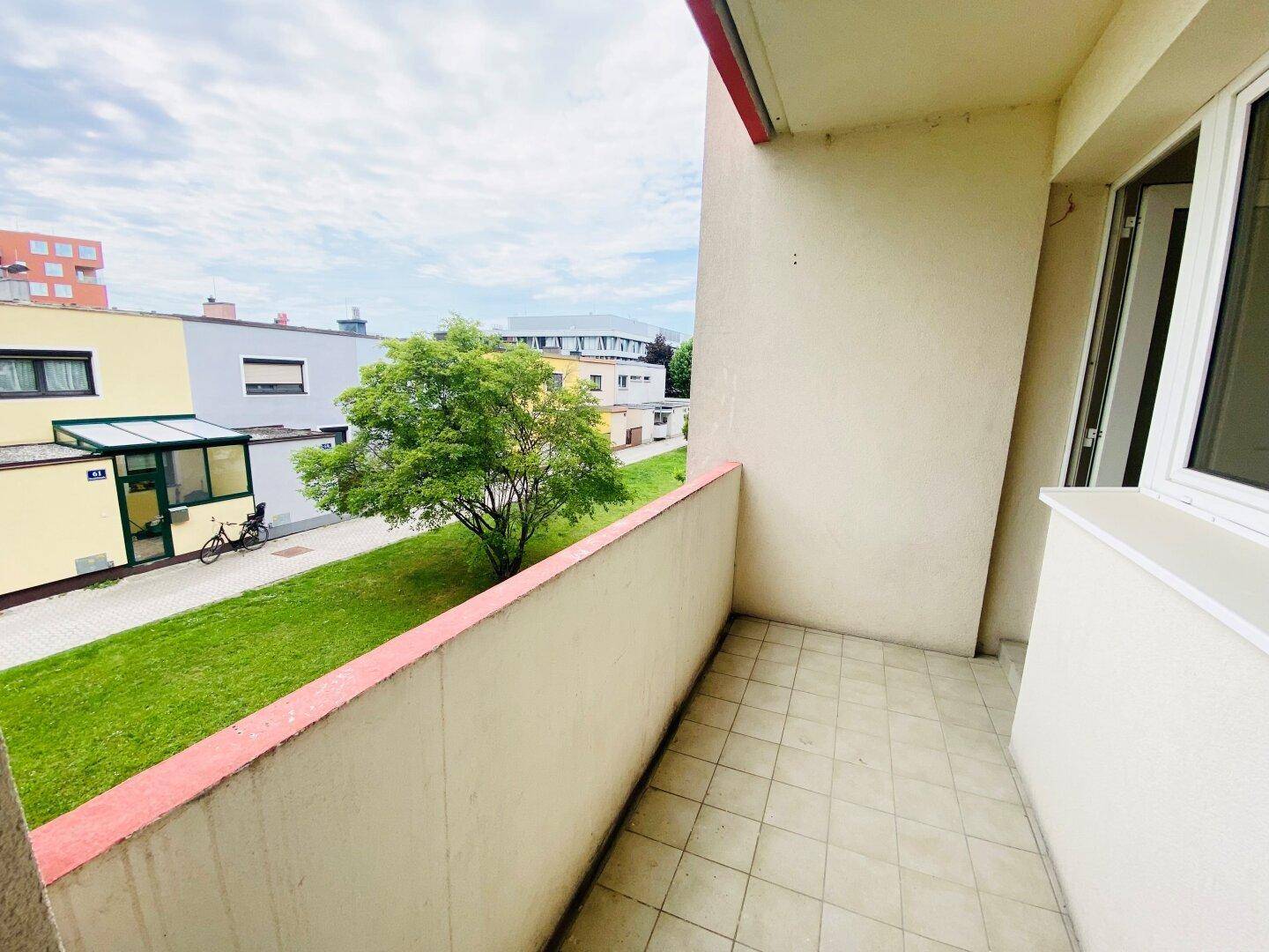 Kleiner Balkon mit Fliesenboden und Blick auf die grüne Umgebung und Nachbargebäude.