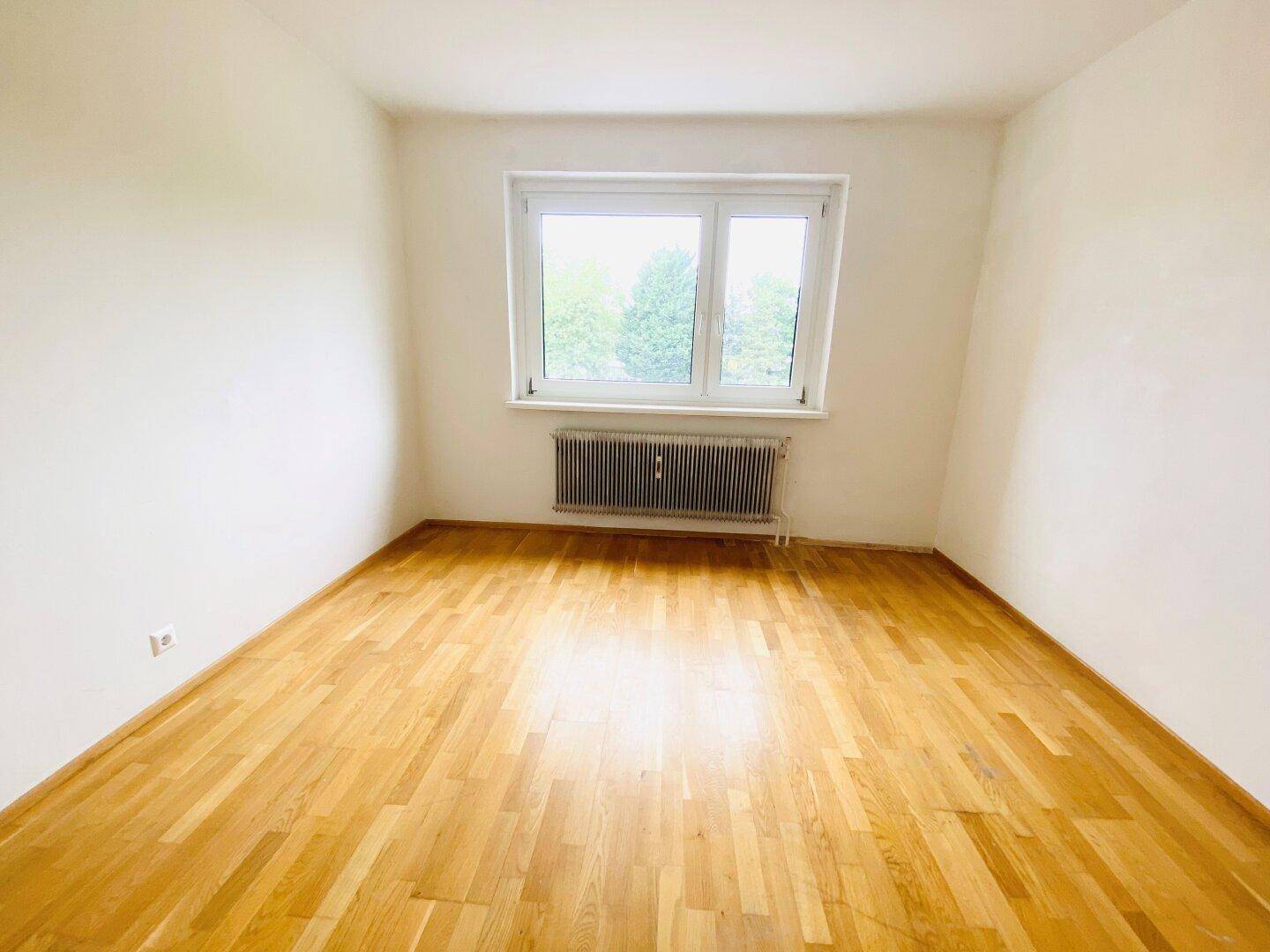 Ruhiges Schlafzimmer mit Parkettboden und Fenster, das einen angenehmen Ausblick bietet.