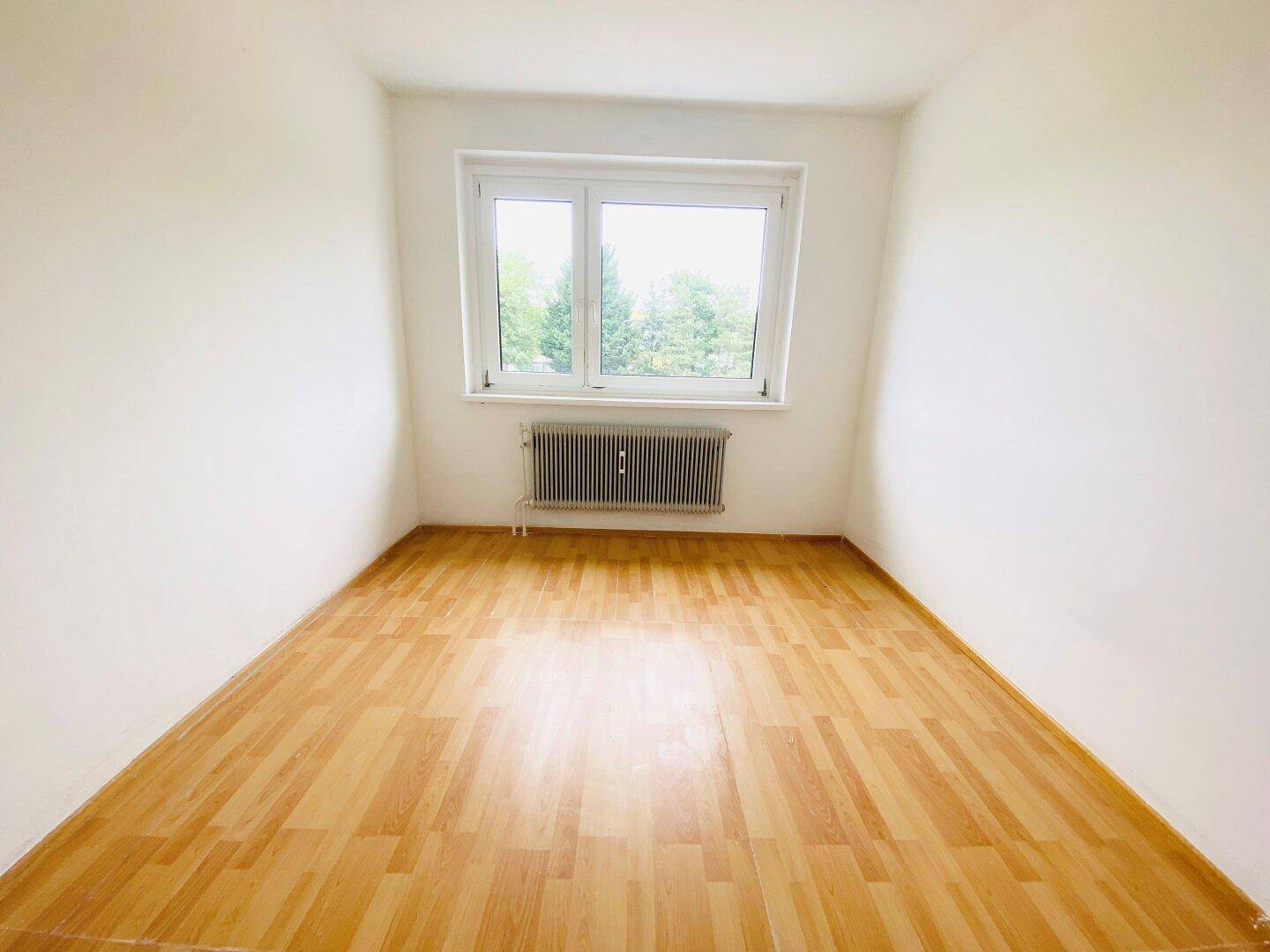 Helles Schlafzimmer mit Parkettboden und Fenster, das viel Tageslicht in den Raum lässt.