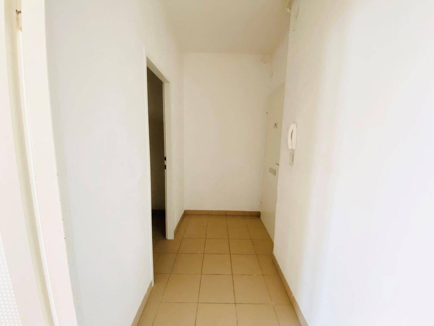Schmaler, heller Flur mit Fliesenboden und Zugang zu einem weiteren Zimmer.