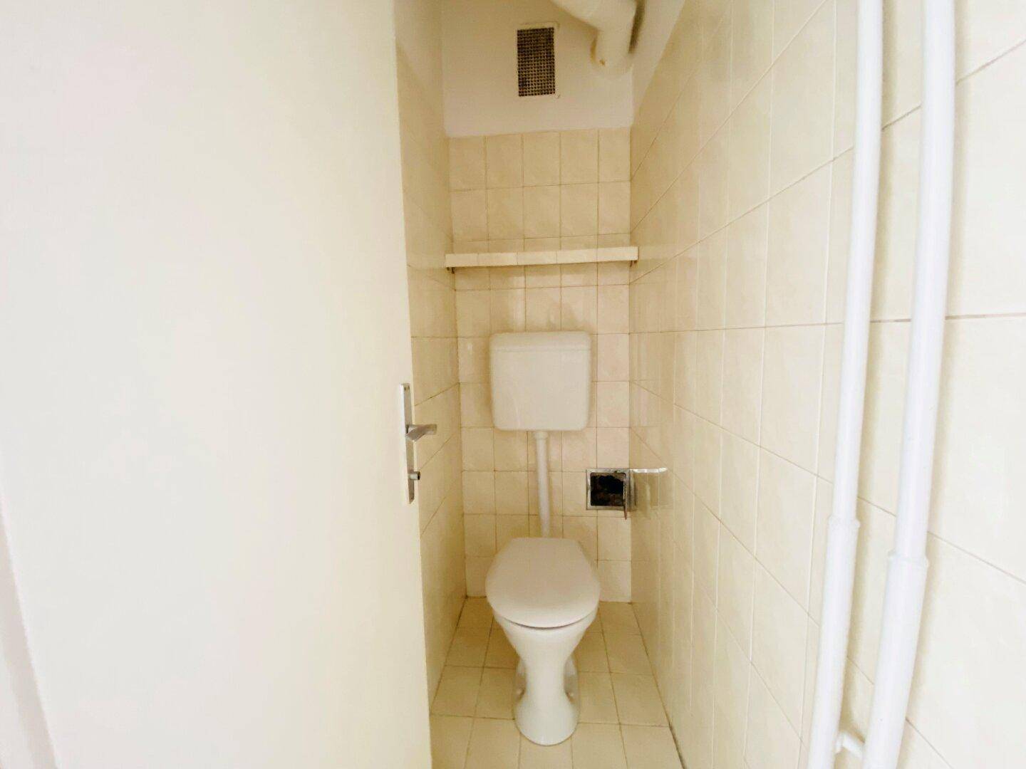 Separate Toilette mit Fliesenboden und Wand-WC in einem kleinen Raum.