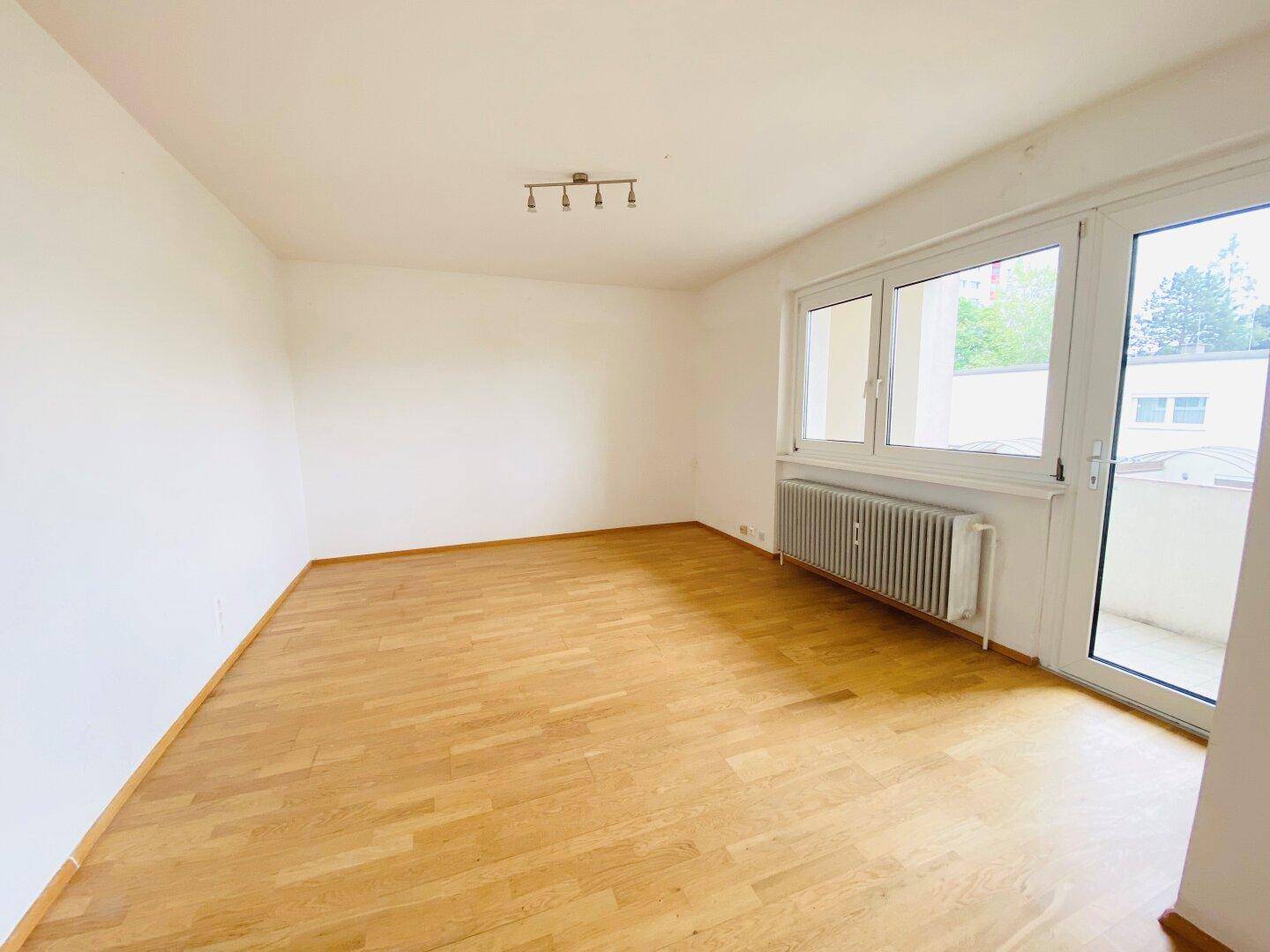 Heller Wohnraum mit Parkettboden und Zugang zu einem Balkon, ideal für Entspannung.