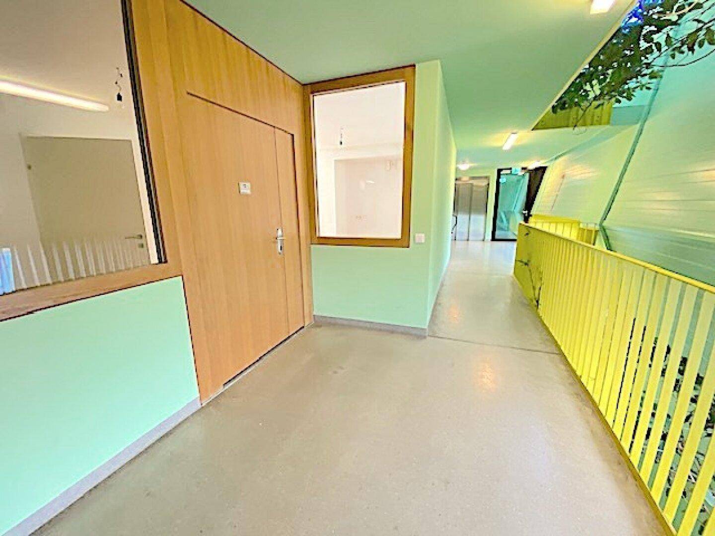 Heller Flur mit Holztüren, Fenster zu einem Nebenraum und grünen Wänden mit Pflanzen.