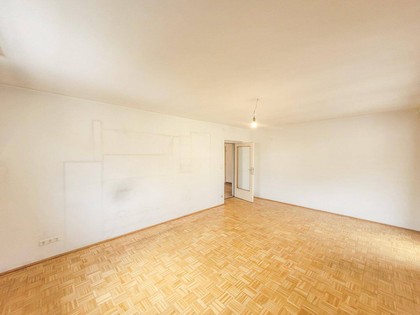 Geräumiges Zimmer mit Parkettboden und einer Tür, die zu einem weiteren Raum führt.