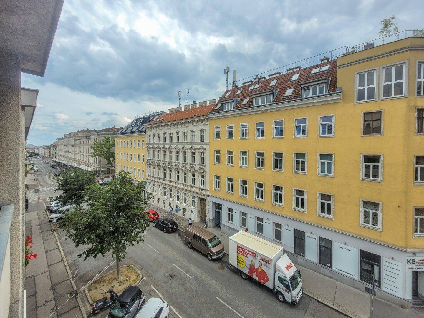 Weitläufiger Blick vom Balkon über die Straße mit parkenden Autos und Gebäuden.