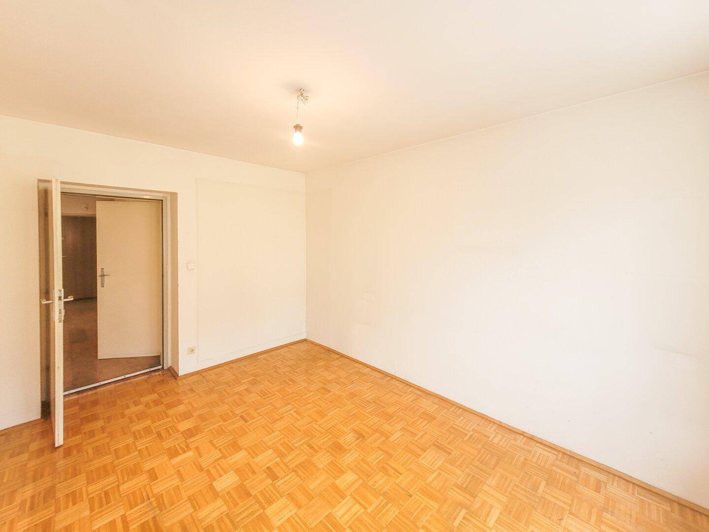 Leeres Schlafzimmer mit Parkettboden und einer geöffneten Tür, die den Zugang ermöglicht.