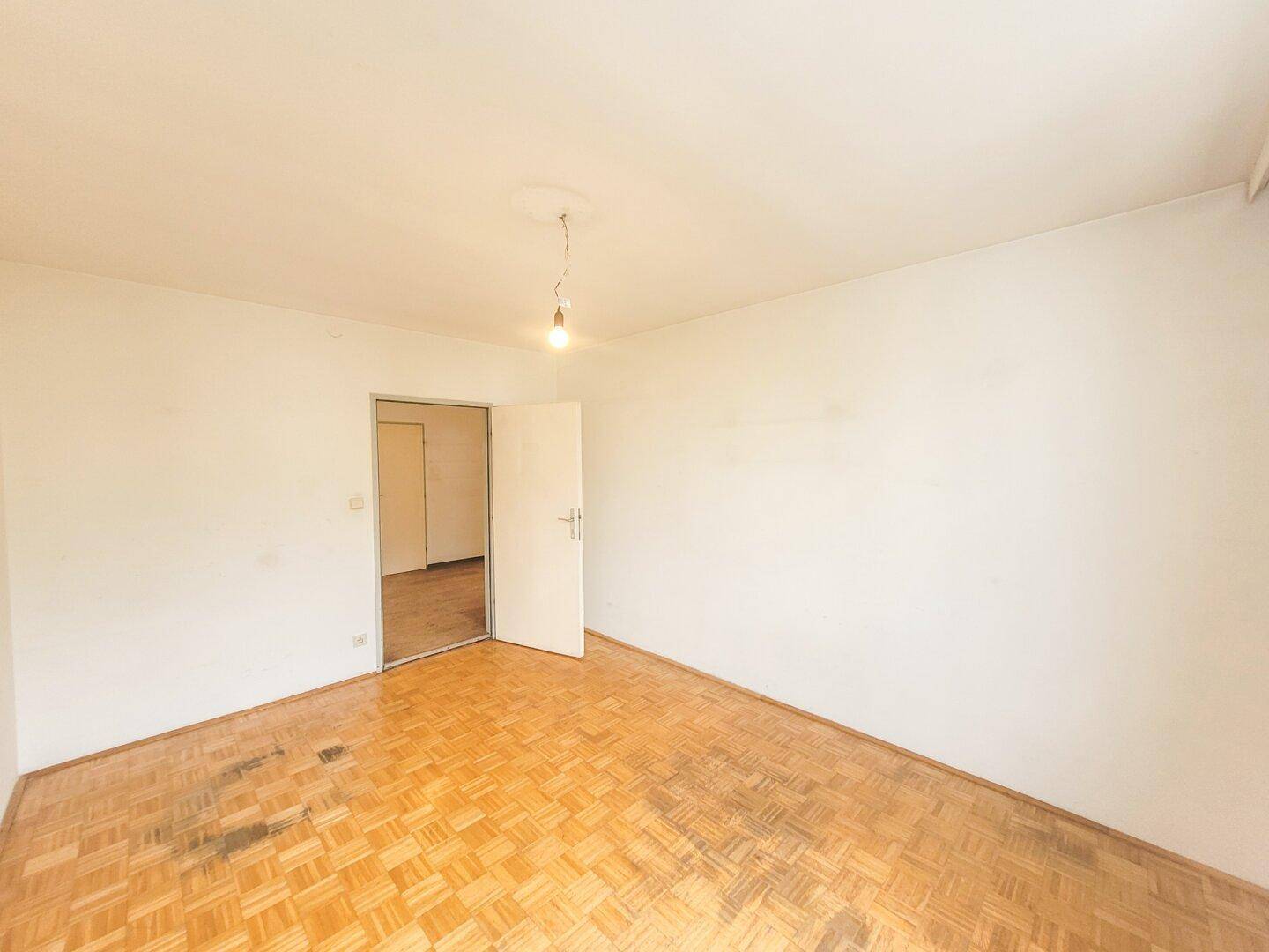 Helles Zimmer mit Parkettboden und einer offenen Tür, die den Raum zugänglich macht.