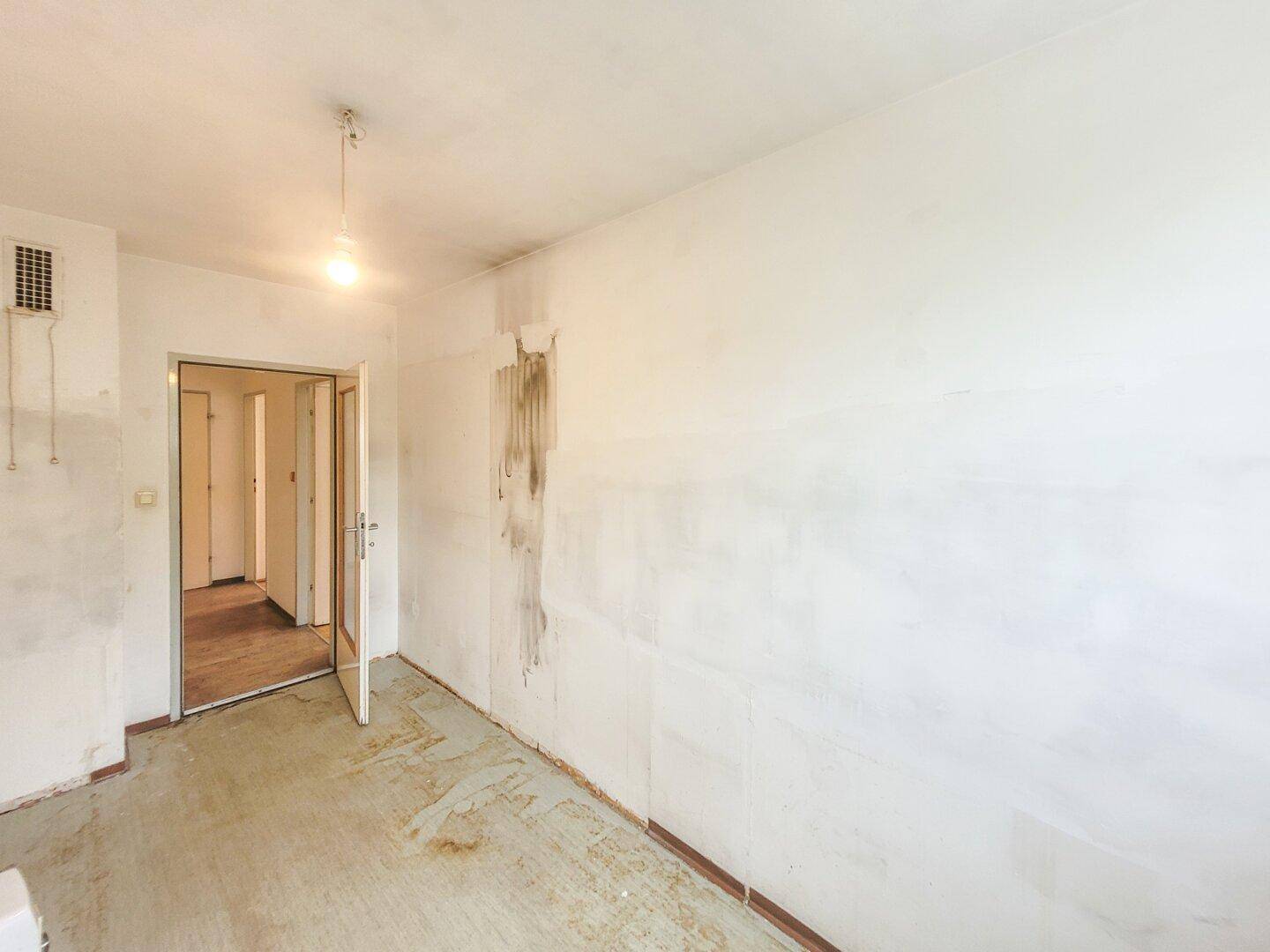 Renovierungsbedürftiger Raum mit freigelegten Wänden und Betonboden, bereit für die Neugestaltung.