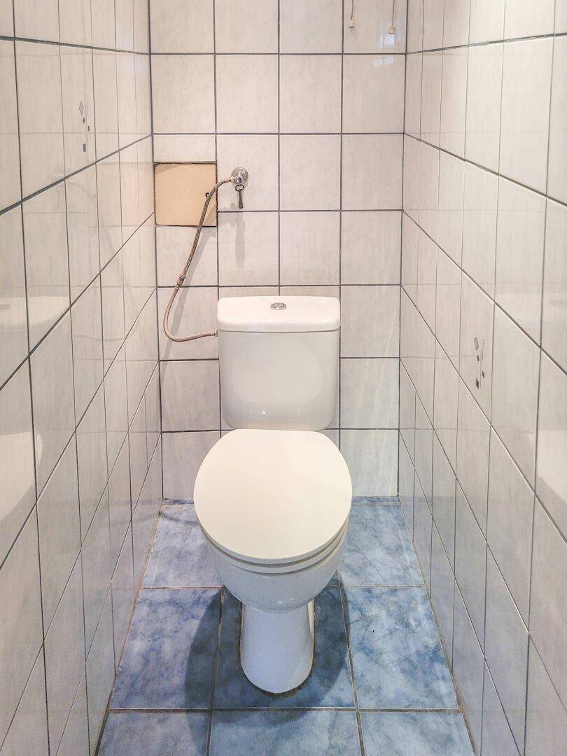 Kleines WC mit Toilette und vollständig gefliesten Wänden und blauem Boden.