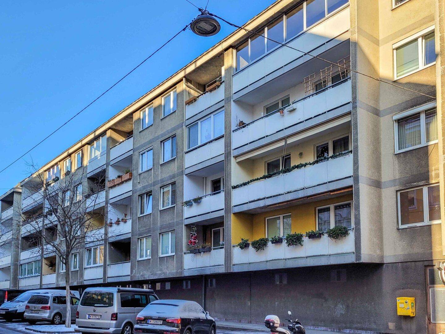 Lange Fassade eines Wohngebäudes mit vielen Balkonen und Fenstern entlang der Straße.