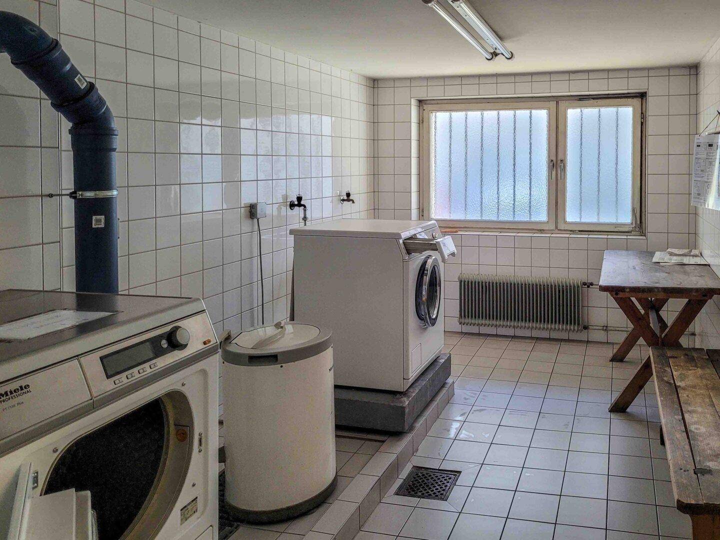 Funktionale Gemeinschaftswaschküche mit Waschmaschinen, Trockner und Fliesenboden.
