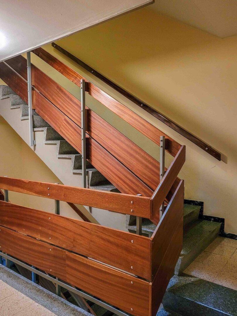 Helles Treppenhaus mit Holzgeländer und Terrazzoboden in einem Mehrfamilienhaus.