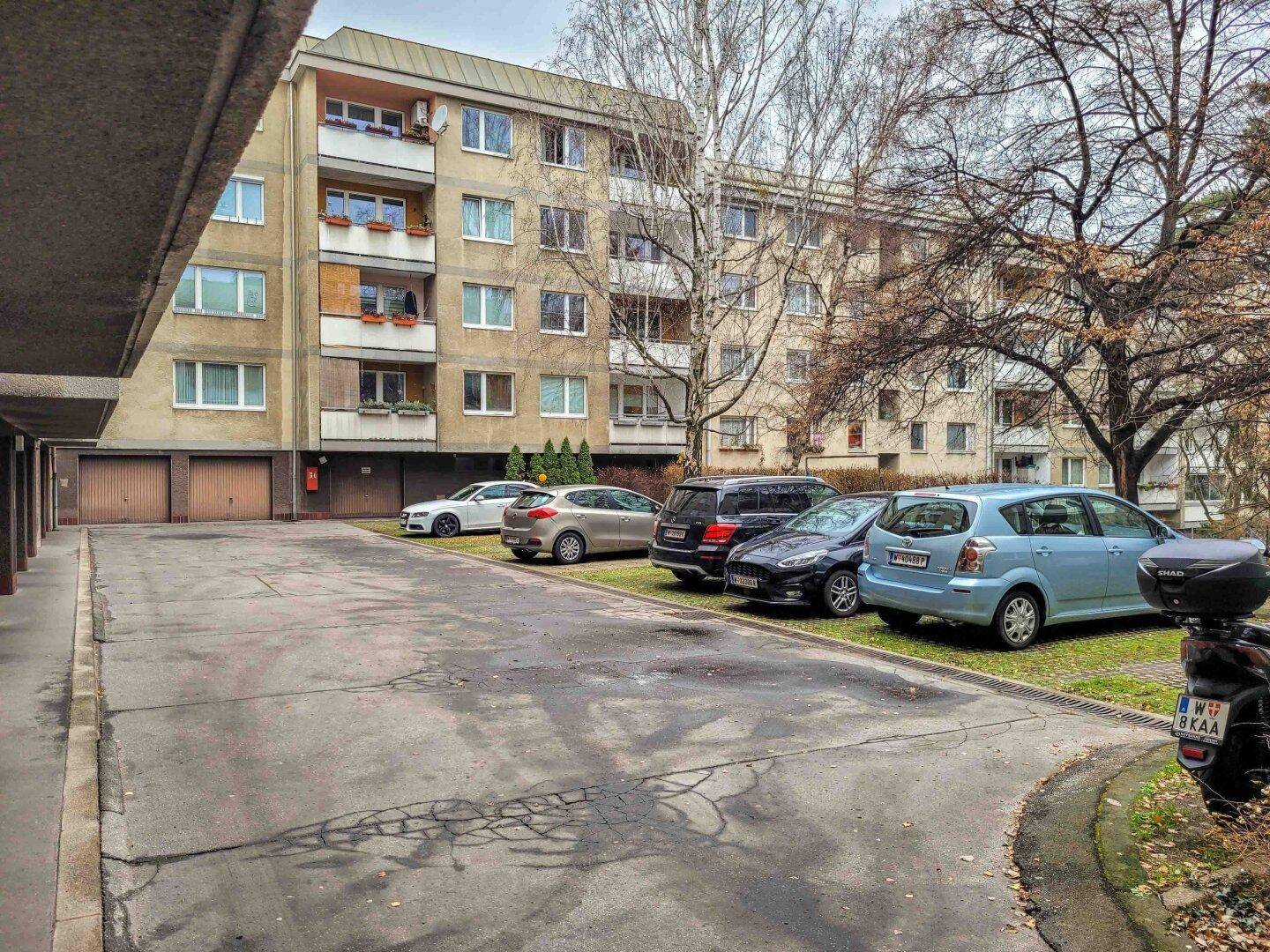 Außenansicht eines Wohngebäudes mit Parkplätzen und Garagen im Erdgeschoss.