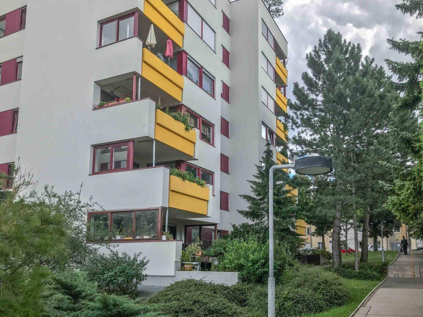 Mehrstöckiges Wohngebäude mit weißer Fassade und gelben Balkonen, umgeben von Grünflächen.