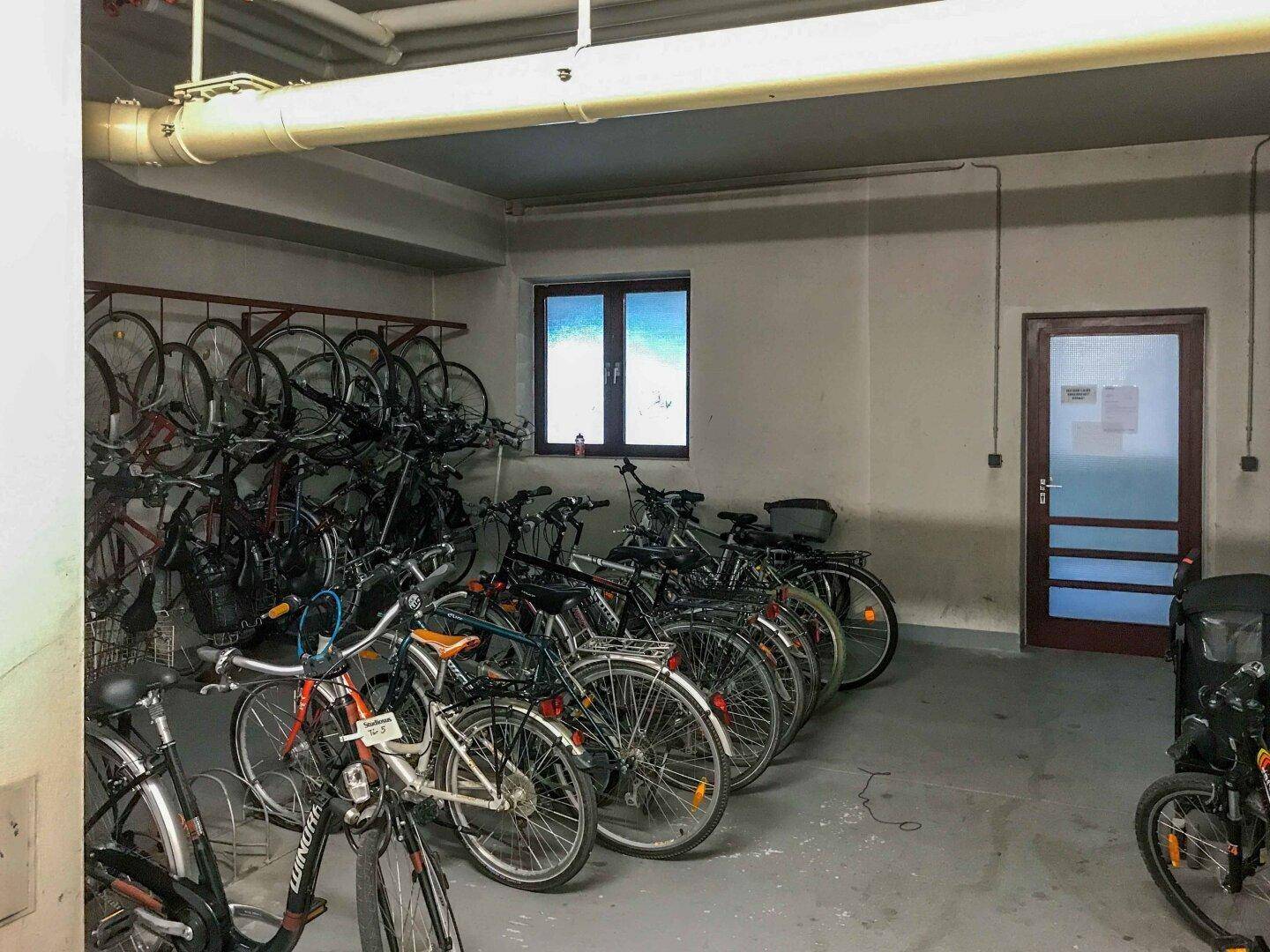 Fahrradabstellraum im Innenbereich mit zahlreichen Fahrrädern und einem Fenster.