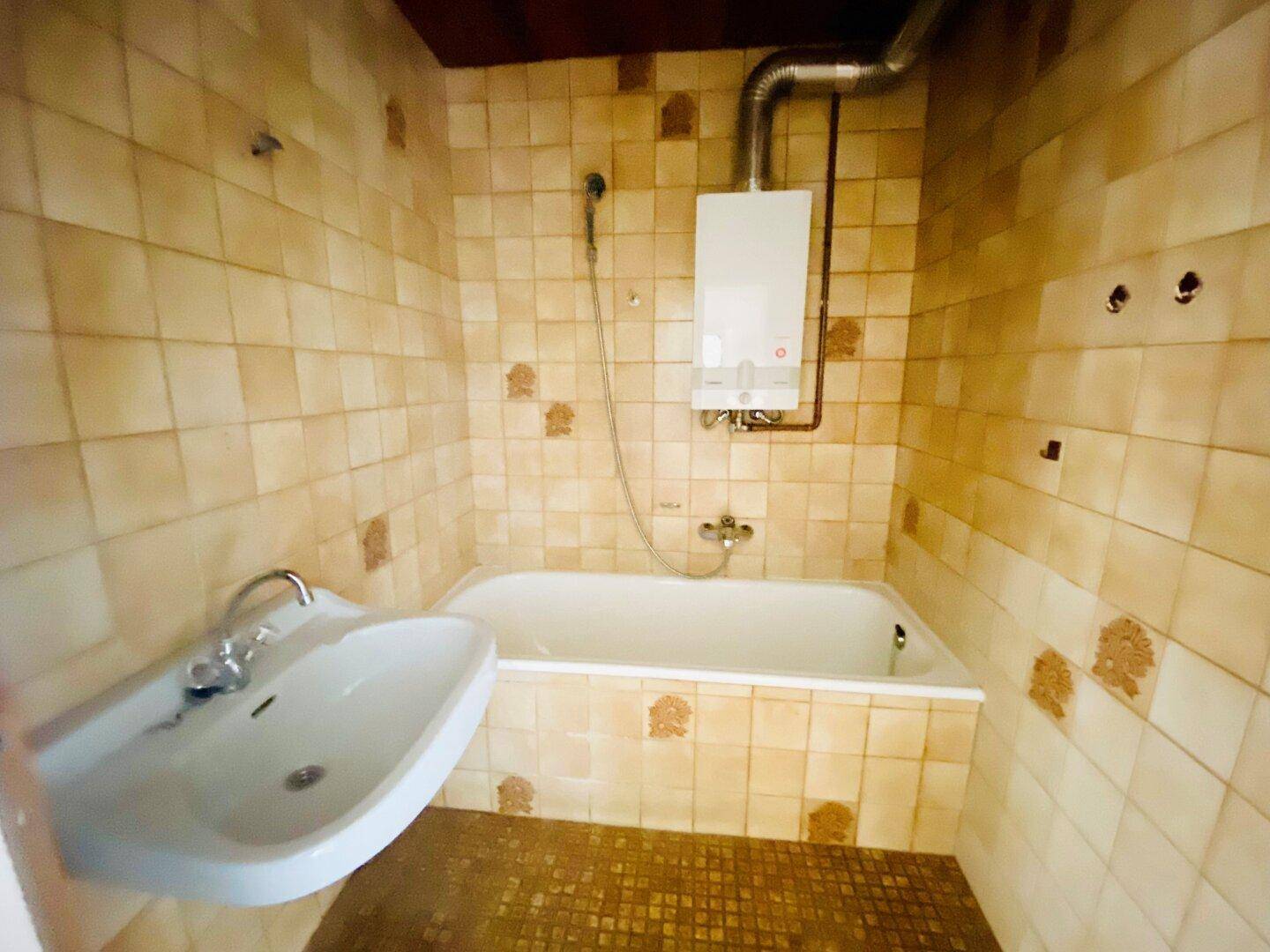 Badezimmer mit Badewanne, Waschbecken und beigefarbenen Fliesen im 80er-Jahre-Stil.