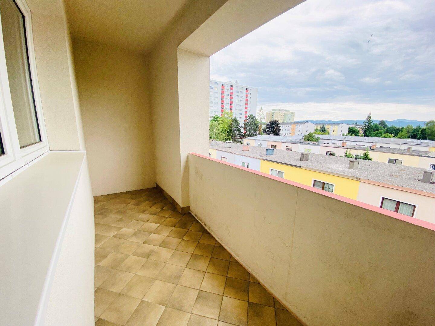 Überdachter Balkon mit Fliesenboden und Blick auf die umliegenden Gebäude und Grünflächen.