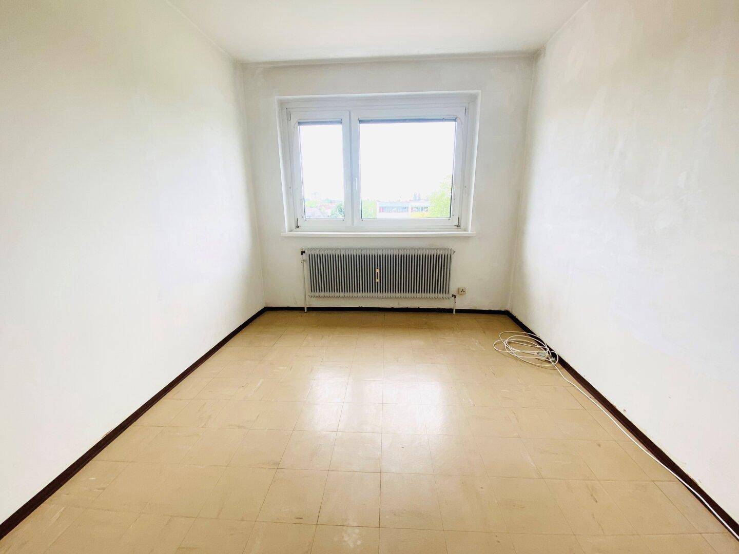Helles Schlafzimmer mit hellem Boden, weißen Wänden und einem Fenster mit Heizkörper.