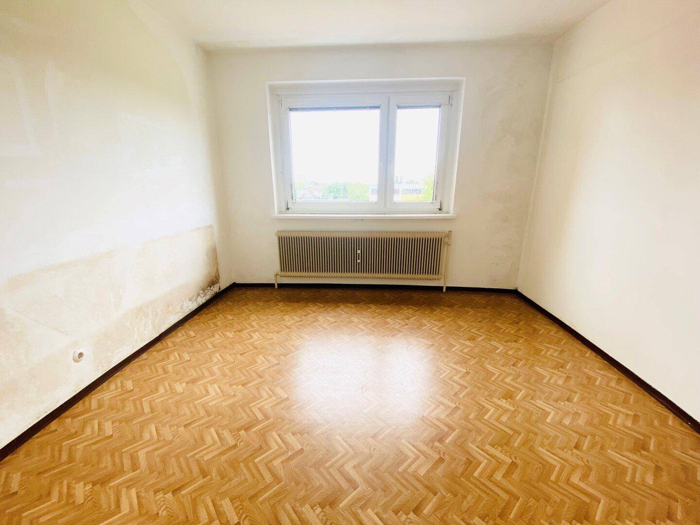 Schlafzimmer mit Fischgrätparkettboden und Fenster, das natürliches Licht hereinlässt.