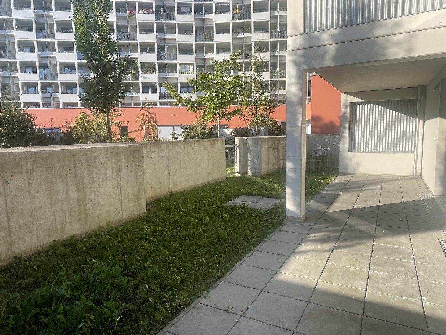 Eine gepflasterte Terrasse mit angrenzender Grünfläche vor einem modernen Mehrfamilienhaus.