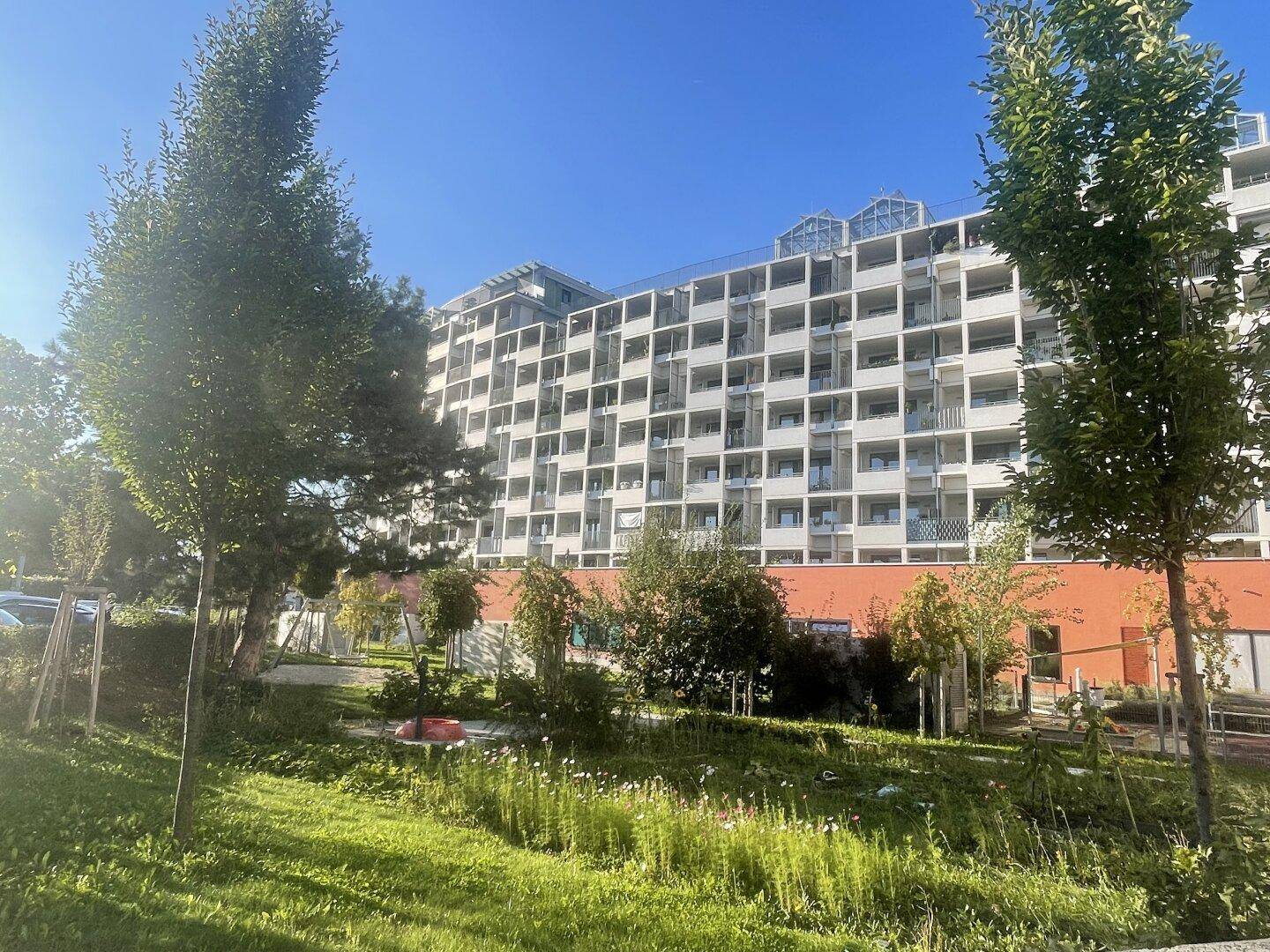 Modernes Mehrfamilienhaus mit zahlreichen Balkonen und grüner Umgebung unter blauem Himmel.