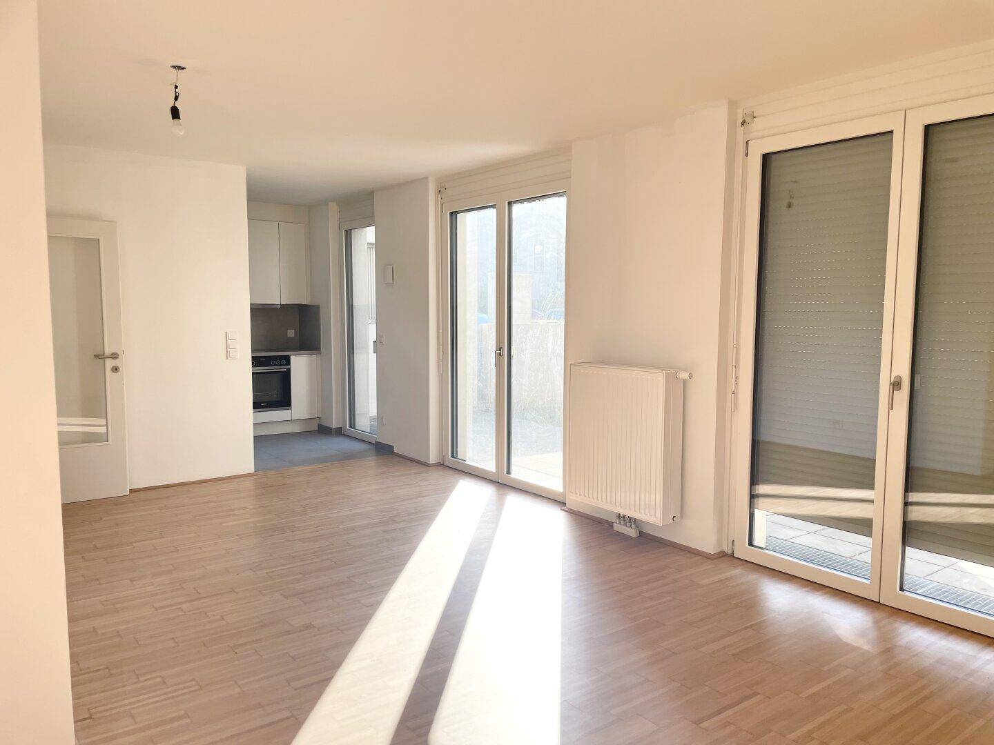 Helles Wohnzimmer mit Parkettboden, großen Schiebetüren und Zugang zu einem Außenbereich.