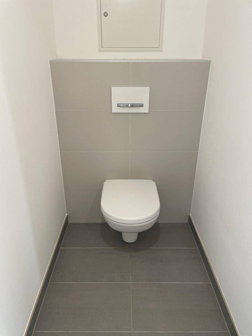 Separates WC mit wandhängender Toilette und modernen Fliesen an Wänden und Boden.