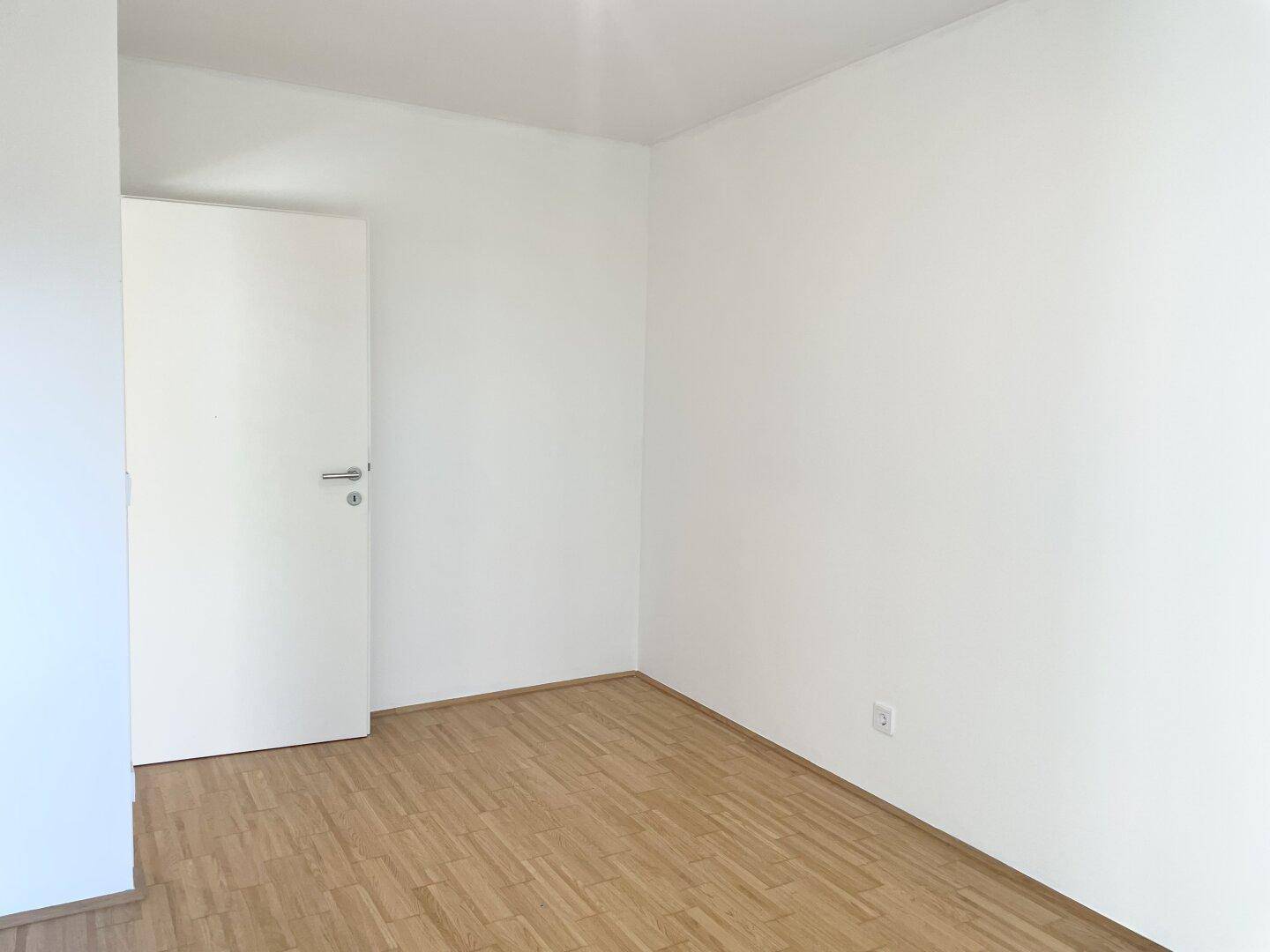Helles Zimmer mit Parkettboden und schlichten weißen Wänden, ideal für ein Schlafzimmer.