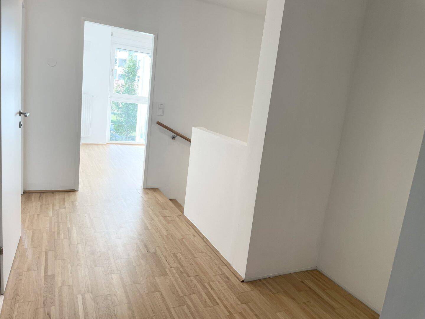 Flur mit Parkettboden und Blick in ein weiteres Zimmer, Treppenaufgang sichtbar.