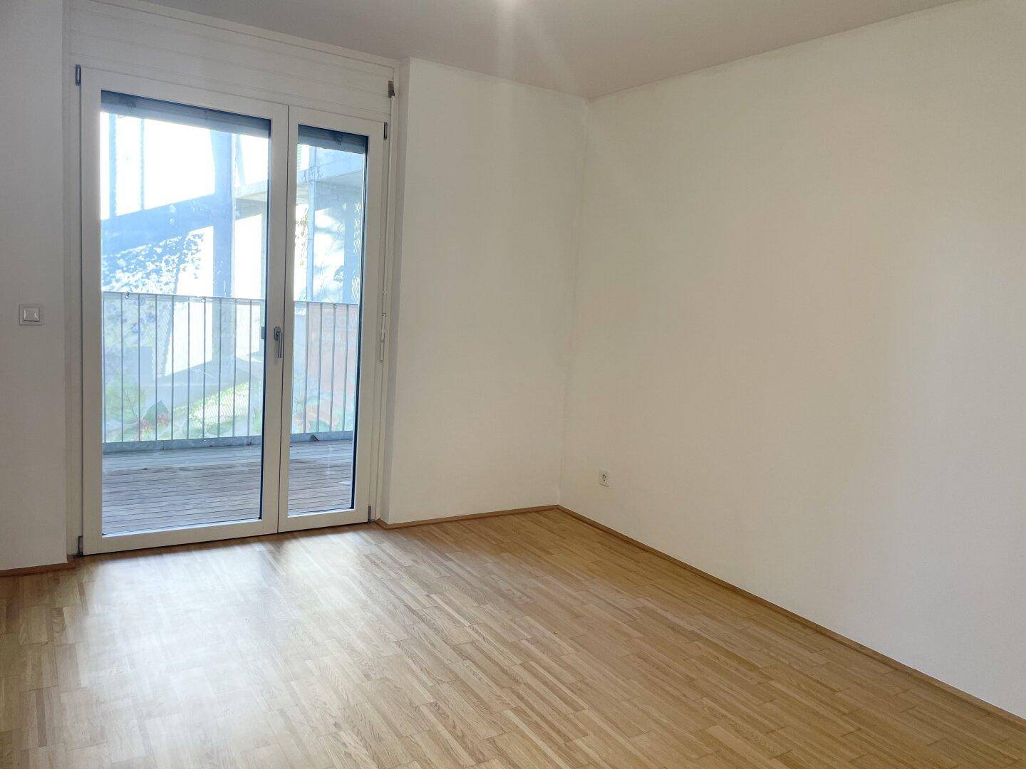 Geräumiges Zimmer mit Parkettboden und Zugang zu einem Außenbereich durch große Glastüren.