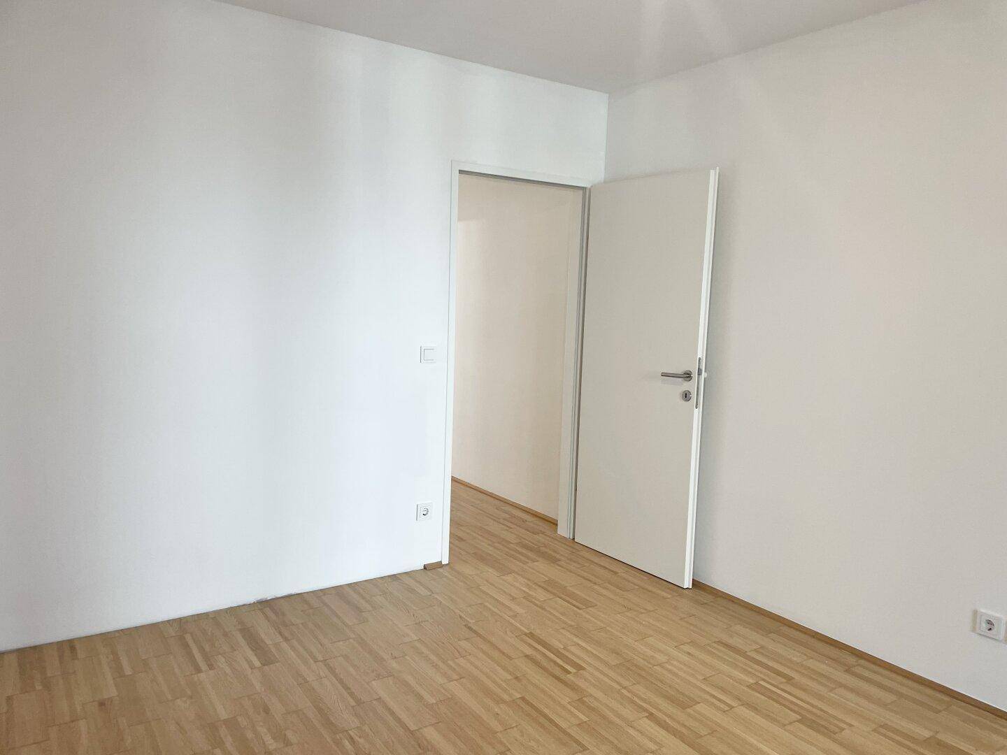 Schlichtes Zimmer mit Parkettboden und weißen Wänden, bietet vielseitige Nutzungsmöglichkeiten.