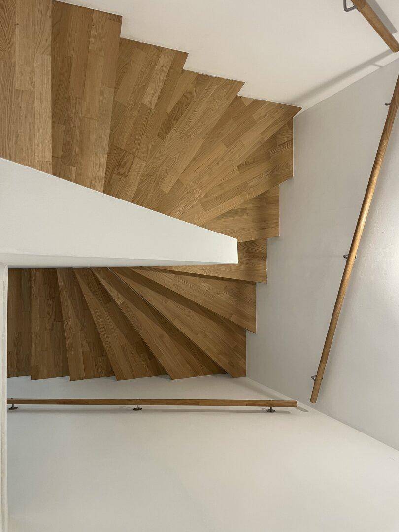 Wendeltreppe mit Holzstufen und Geländer, die die Stockwerke verbindet.