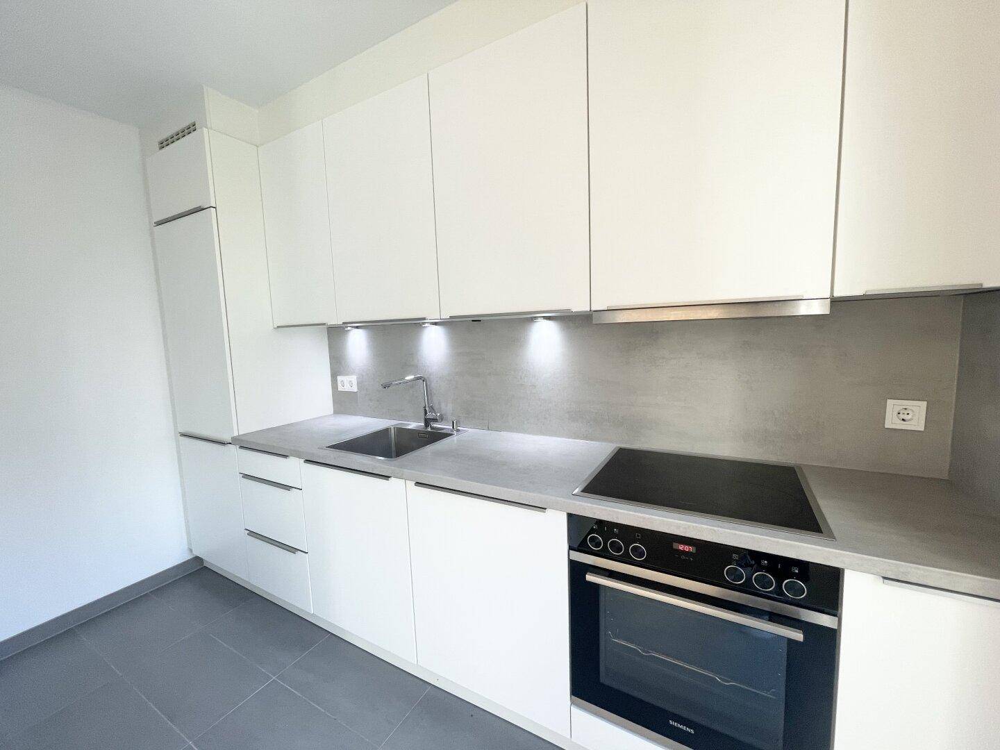 Moderne Einbauküche mit weißen Schränken, grauen Arbeitsplatten und integrierten Geräten.