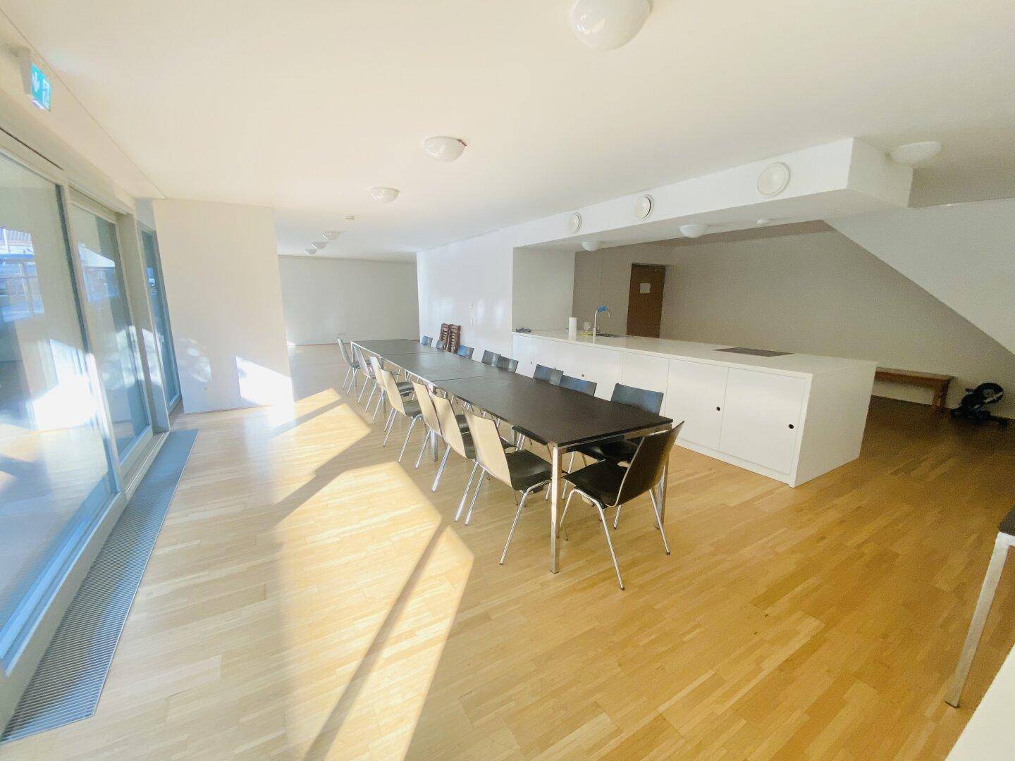Heller, offener Wohn- und Essbereich mit langer Tafel, moderner Küchenzeile und großen Fenstern.
