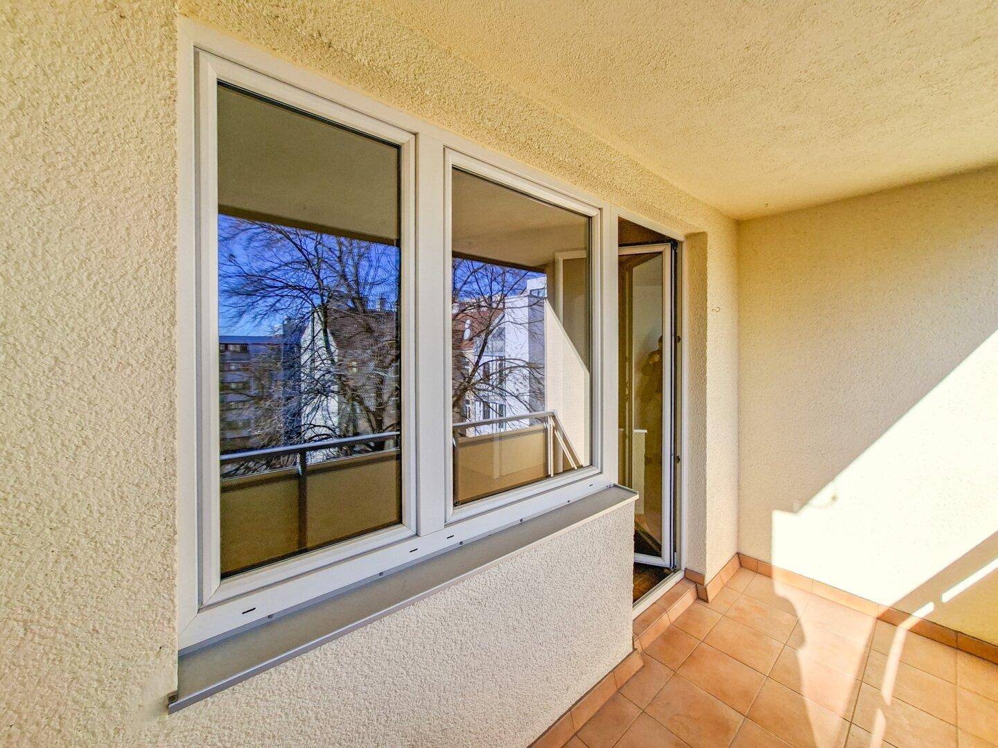 Balkon mit Fliesenboden und Blick durch die Fenster in einen Innenraum.